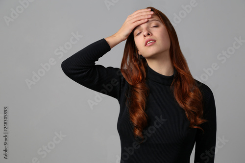 Φωτογραφία The redhead girl tired and has a headache at gray background