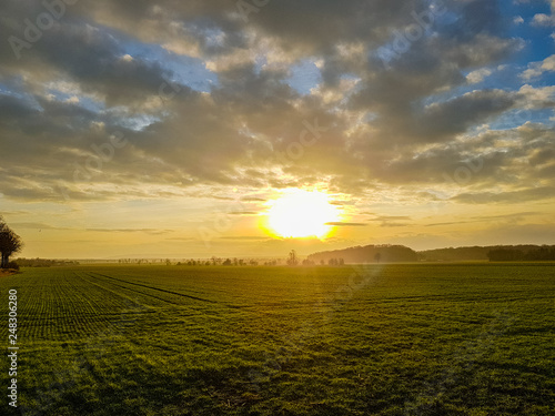 Sunset on the cloudy sky over a green field, mountains in the back