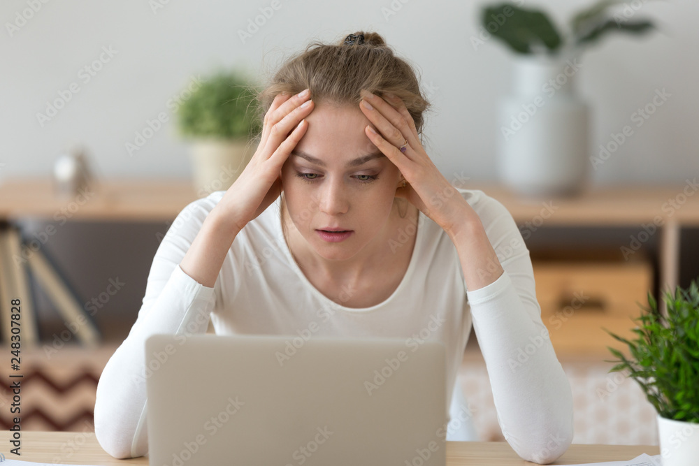 Stressed young woman looking at laptop reading bad internet news Stressed young woman looking at laptop reading bad internet news