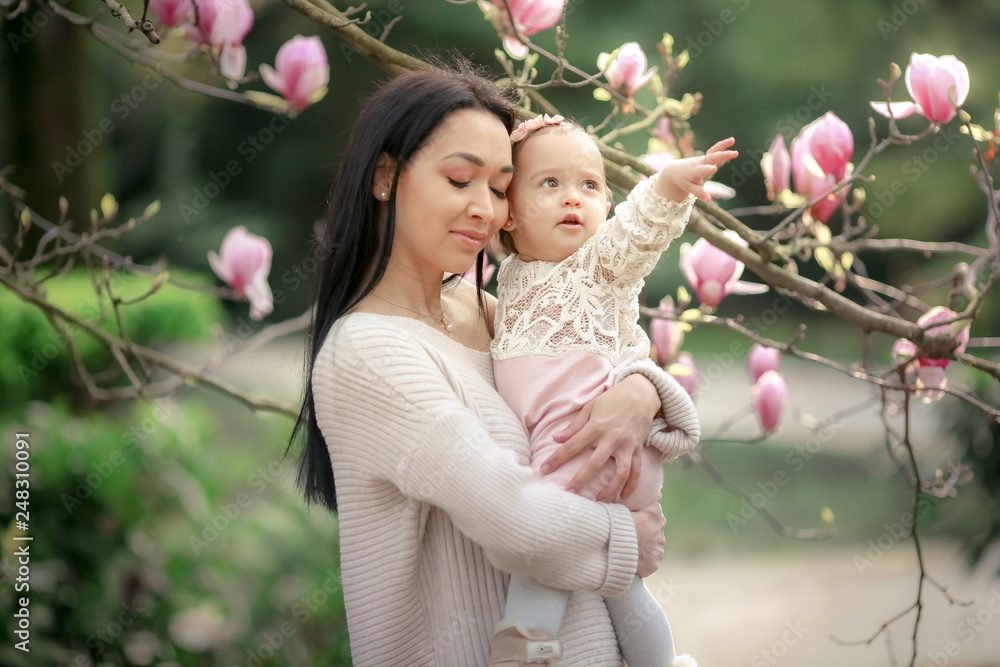 Fototapeta premium Young mother and little daughter in autumn park play with magnolia leaves. Happy weekend with family in autumnal forest park. People in park. Smiling woman and baby in outdoor. Fall. Sunny day