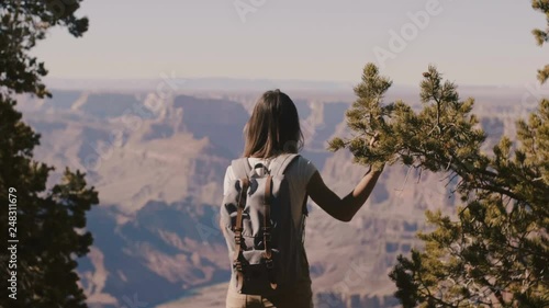 Beautiful young happy tourist woman with backpack watching epic Grand Canyon mountains, walking back to camera.