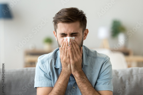 Ill young man sneezing in handkerchief blowing wiping running nose photo
