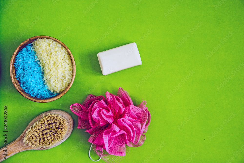 Cosmetology, spa beauty products, beauty concept and bikini. Washing facilities, wooden soft massage brush for body and feet, washcloth, soap, colorful sea salt on a green background. Cosmetology, spa beauty products, beauty concept and bikini. Washing facilities, wooden soft massage brush for body and feet, washcloth, soap, colorful sea salt on a green background.