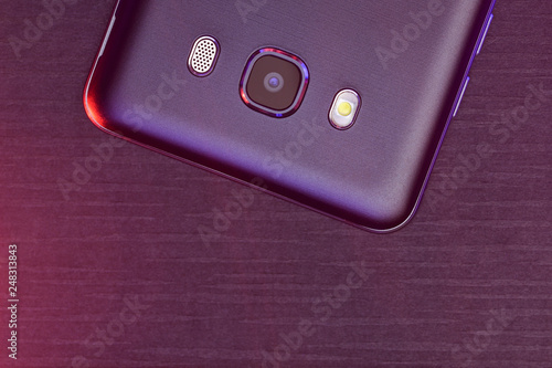 .A fragment of the cell phone case in black with pink and purple backlight. The phone is on black tech ribbed surface camera pink up lighting. .