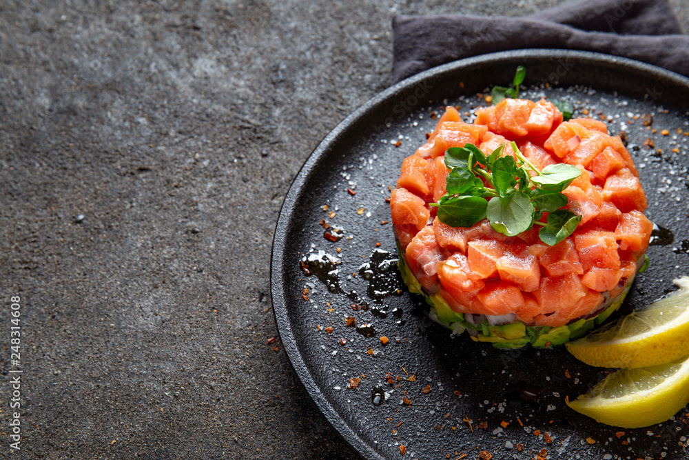 Raw salmon, avocado purple onion salad served in culinary ring on black plate. Black concrete background Raw salmon, avocado purple onion salad served in culinary ring on black plate. Black concrete background