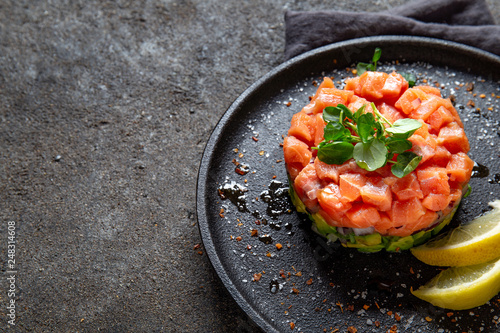 Fotografía Raw salmon, avocado purple onion salad served in culinary ring on black plate