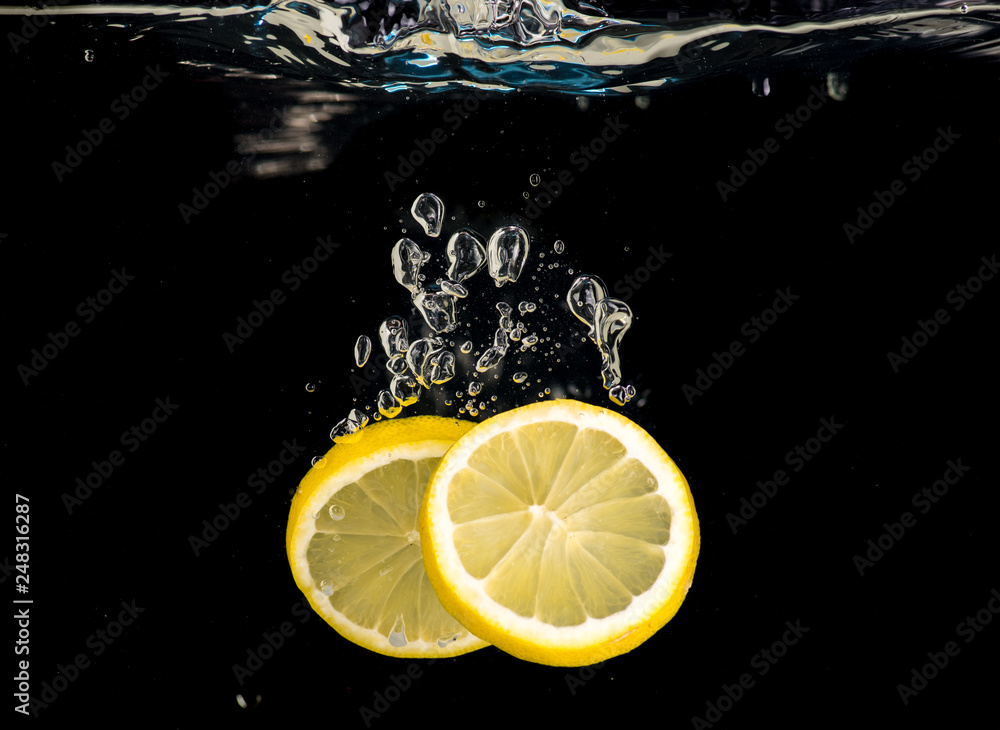 Slices of lemon thrown into water on a black background