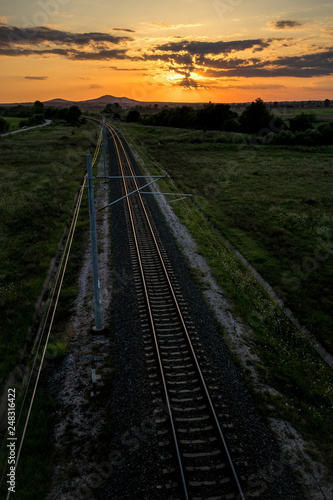 Long empty railway tracks as viewed from a bridge above at summer sunset behind clouds, dark colorful photograph taken near Krum, Bulgaria