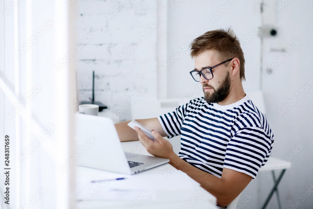 Freelancer man at work in office and looking at open laptop workstation.