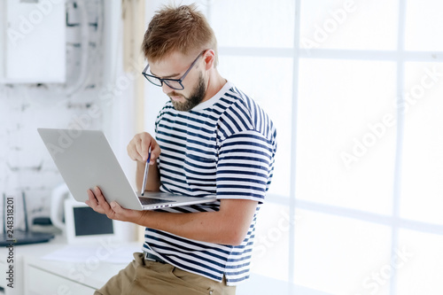 Successful businessman. Office worker. Portrait of bearded businessman. Serious businessman. Man standing at table and holds laptop. Handsome bearded office worker.
