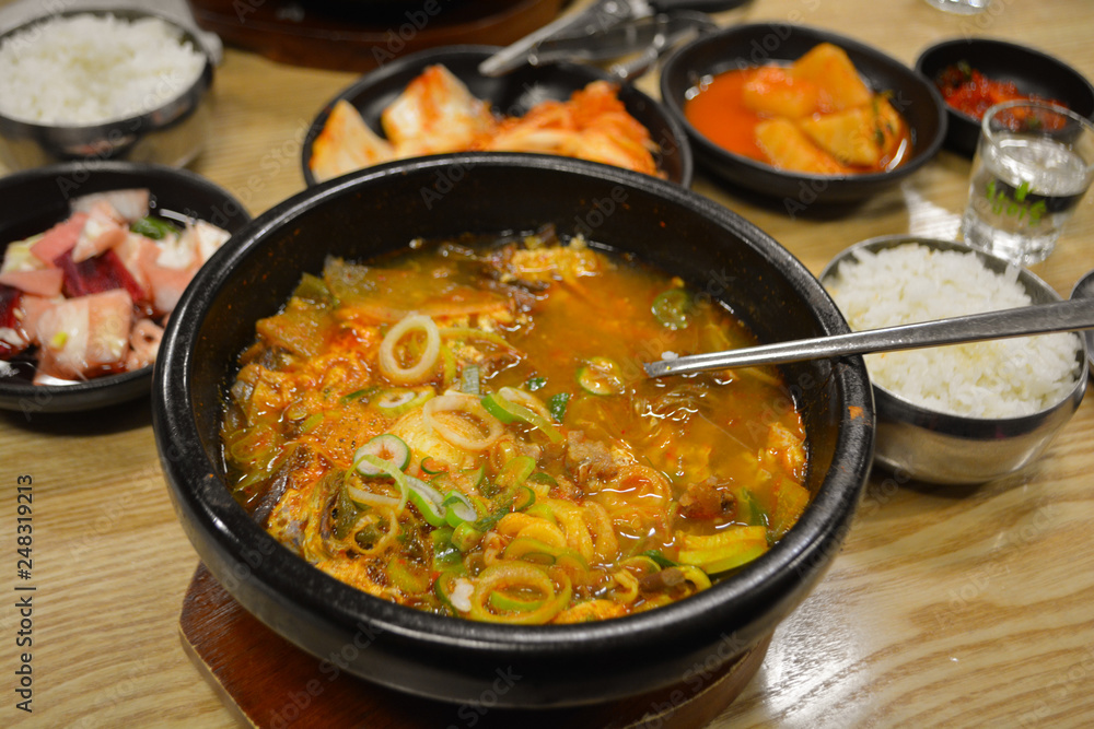 Spicy korean soup with kimchi in background with long korean spoon