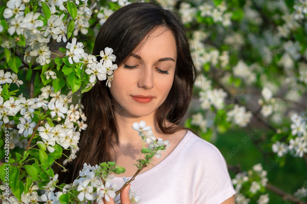 Portrait of brunette girl in springtime. Beautiful young woman in white flowers enjoying apple orchard. Portrait of brunette girl in springtime. Beautiful young woman in white flowers enjoying apple orchard.