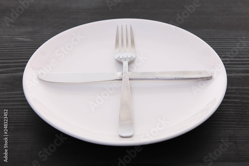 黒い木製テーブルに置かれた白い皿とカトラリーによる次の料理を待機の合図