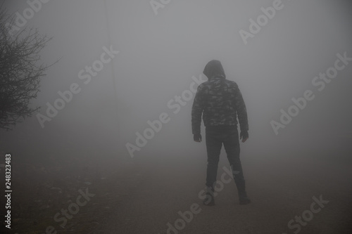 silhouette of a man standing in the foggy road.