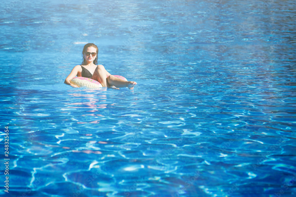 Young pretty girl sails on a floating ring in the pool with clean, blue water in the resort hotel. The concept of recreation and healthy lifestyle.