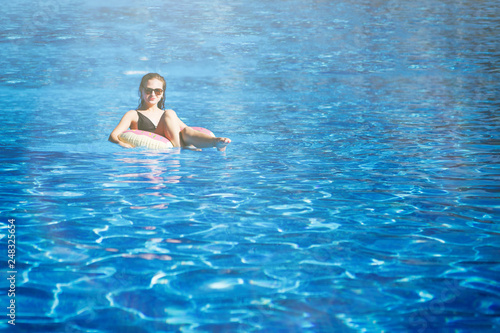 Young pretty girl sails on a floating ring in the pool with clean  blue water in the resort hotel. The concept of recreation and healthy lifestyle.