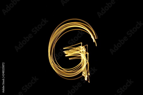 Long exposure, light painting photography.  Letter g in a vibrant neon metallic yellow gold colour against a black background.  Alphabet series.