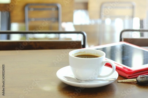 Hot coffee in a white glass is served in front of the tablet and car keys while customers are waiting for an appointment.
