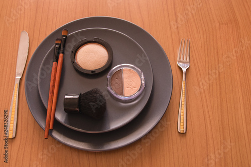 minimal concept background with make up, brushes and powders, on a grey plate, next to cutlery on a wooden table