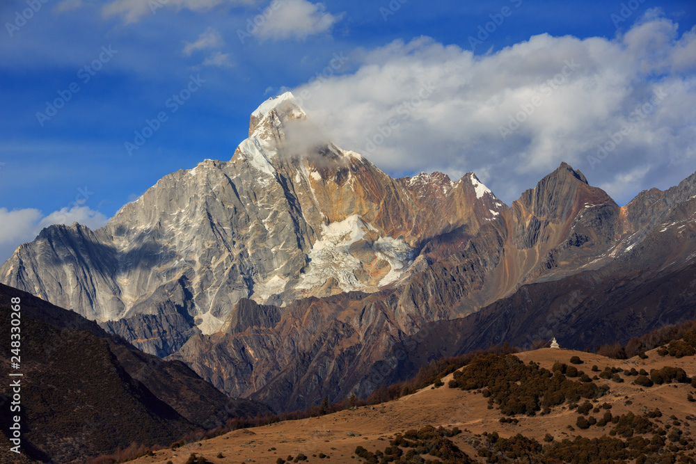 Four Girls Mountain National Park near Xiaojin, Sichuan Province China. Yaomei Peak Summit, blue sky and clouds, White Tibetan Stupa on top of hill in foreground. Mount Siguniang, Hiking Destination Four Girls Mountain National Park near Xiaojin, Sichuan Province China. Yaomei Peak Summit, blue sky and clouds, White Tibetan Stupa on top of hill in foreground. Mount Siguniang, Hiking Destination