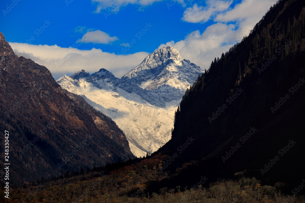 Four Girls Mountain National Park in Sichuan Province, China. ShuangQiao Valley Scenic Area, Snow Capped Jagged Mountains with clouds forming at the summit. Blue Sky, Snow Mountains, Siguniangshan Four Girls Mountain National Park in Sichuan Province, China. ShuangQiao Valley Scenic Area, Snow Capped Jagged Mountains with clouds forming at the summit. Blue Sky, Snow Mountains, Siguniangshan