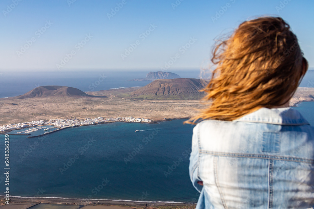 A woman stands on the edge of a cliff and looks at a nearby island in the ocean.