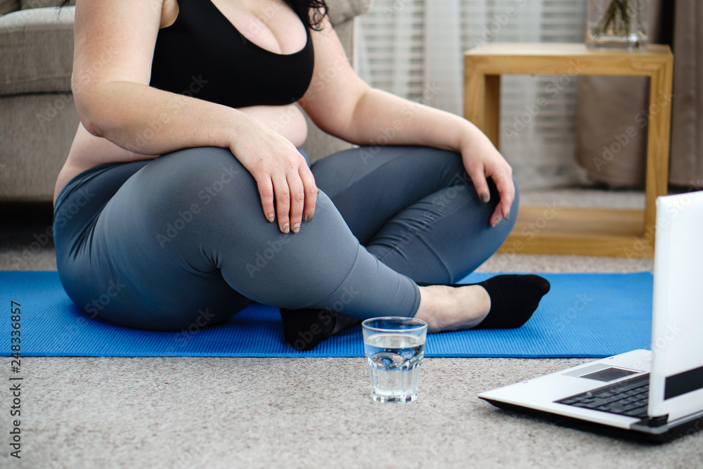 fitness, online personal trainer, home training, technology and diet. overweight woman practicing yoga at home, drinking water, taking a break between sets