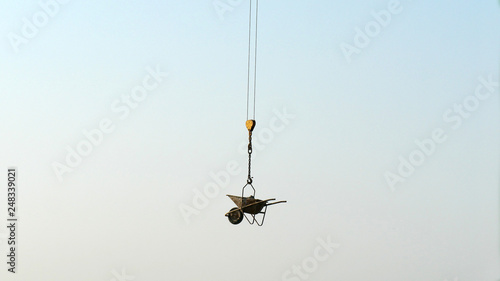 Wheelbarrow hanging on a crane during a building renovation. sky background.