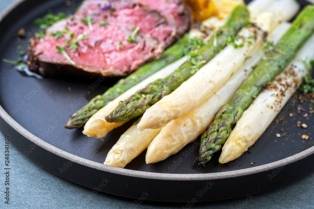 Traditional white and green asparagus with barbecue dry aged sliced beef fillet and fried potatoes served as closeup on a modern design plate Traditional white and green asparagus with barbecue dry aged sliced beef fillet and fried potatoes served as closeup on a modern design plate