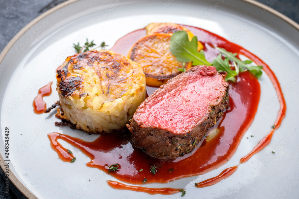 Traditional saddle of venison with Swiss rösti, quince and orange slices in game red wine sauce as closeup on a modern design plate Traditional saddle of venison with Swiss rösti, quince and orange slices in game red wine sauce as closeup on a modern design plate