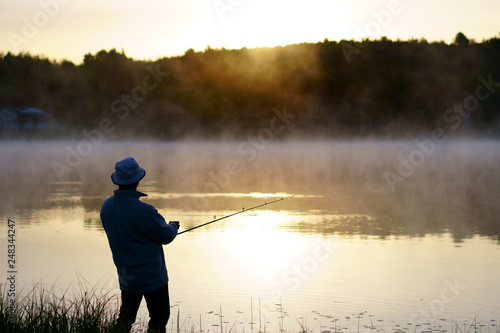 Caucasian fisherman, 50's, at the lake with fog, early morning just before sunrise.