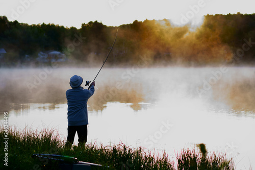 Caucasian fisherman, 50's, at the lake with fog, early morning just before sunrise.
