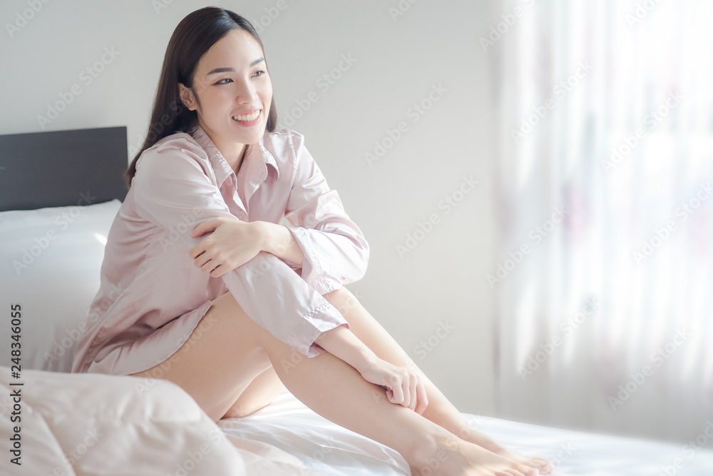 sexy women wearing pink pajamas, sitting and laughing on the bed in the morning. beautiful girl smile