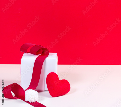 White gift box and red heart shaped fabric and white pom pom with red ribbon