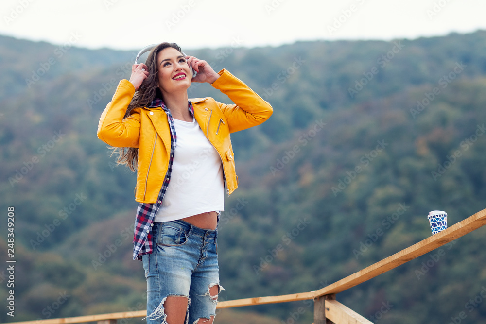 Adorable long hair girl standing at the wooden bridge with forest on the background with headphones on her head Adorable long hair girl standing at the wooden bridge with forest on the background with headphones on her head