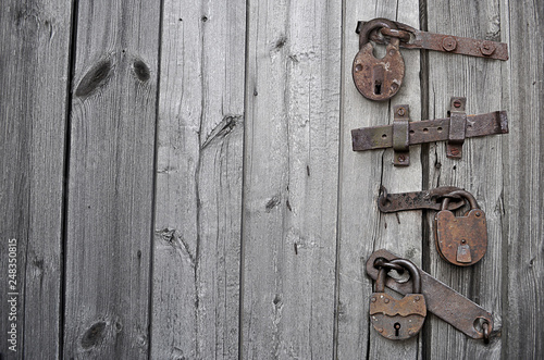 The wooden door is closed with a bolt and rusty locks