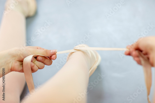 Focus on ballet dancer legs who tie shoelace while sitting on the floor