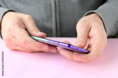 Male hands are holding a phone and putting on a shiny colorful cover. White man in a gray sweater put on a new violet case on smartphone with selective focus. Plastic case for digital gadget