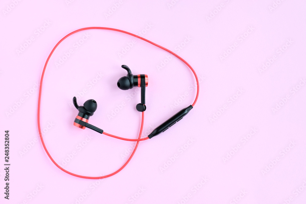 Wireless bluetooth red earphones with selective focus on neutral pink background. Smart digital sound personal headset. Mobile music stereo headphones. Portable gadget for listening music Wireless bluetooth red earphones with selective focus on neutral pink background. Smart digital sound personal headset. Mobile music stereo headphones. Portable gadget for listening music