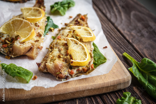 Baked pollock fillet with lemon and spinach on a wooden background