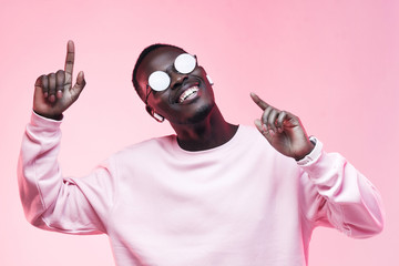 Young smiling african american man listening to music with earphones, dancing isolated on pink background