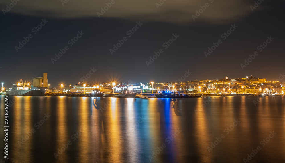 Cityscape of the Mediterranean port of Cagliari seen from the sea. Port of Cagliari during a night full of clouds.
