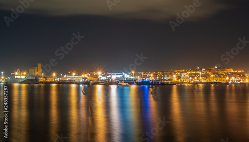 Cityscape of the Mediterranean port of Cagliari seen from the sea. Port of Cagliari during a night full of clouds.