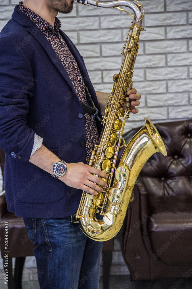 Naklejka premium men's hands holding a saxophone against a white wall and a leather sofa