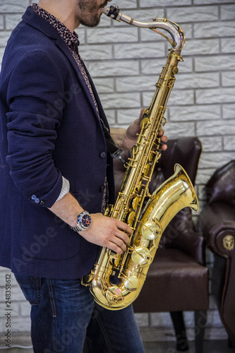men's hands holding a saxophone against a white wall and a leather sofa