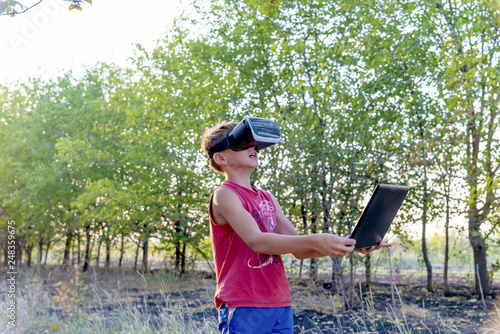 A boy on nature in virtual space, VR glasses, a forest, a laptop. © andov