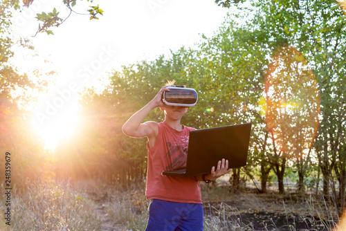 A boy on nature in virtual space, VR glasses, a forest, a laptop. © andov