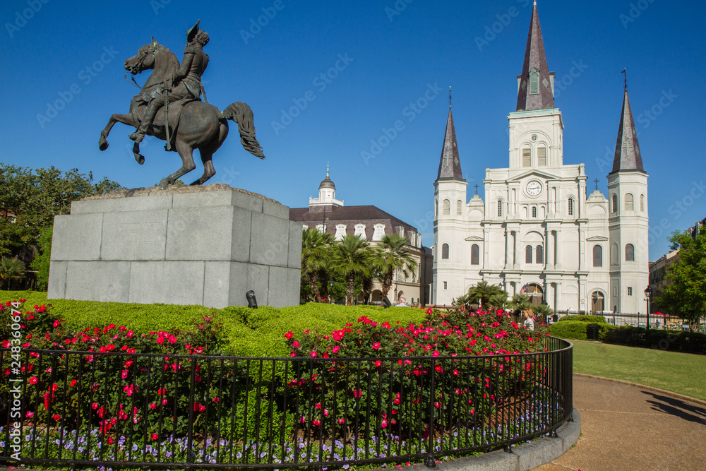 Fototapeta premium St. Louis Cathedral, Jackson Square, Louisiana, United States. Color horizontal image with Andrew Jackson statue in foreground with red flowers.