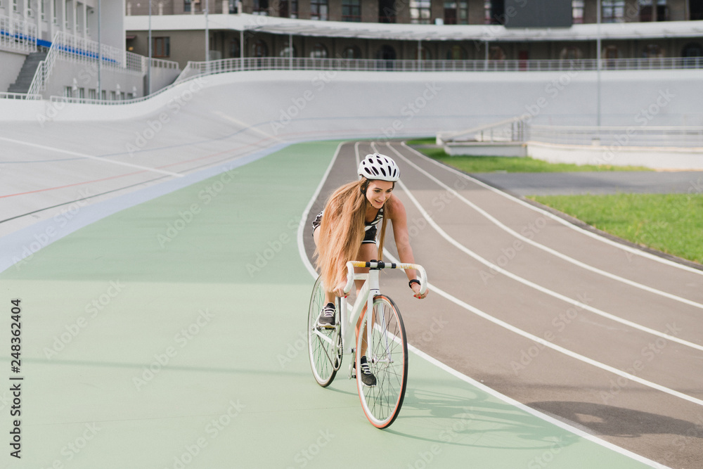 Fototapeta premium Cycling and fitness. Young beautiful fit woman with perfect body in sportswear on the bicycle outdoors on the track. Sportive and healthy lifestyle, cyclist working out, training, fashion, beauty.