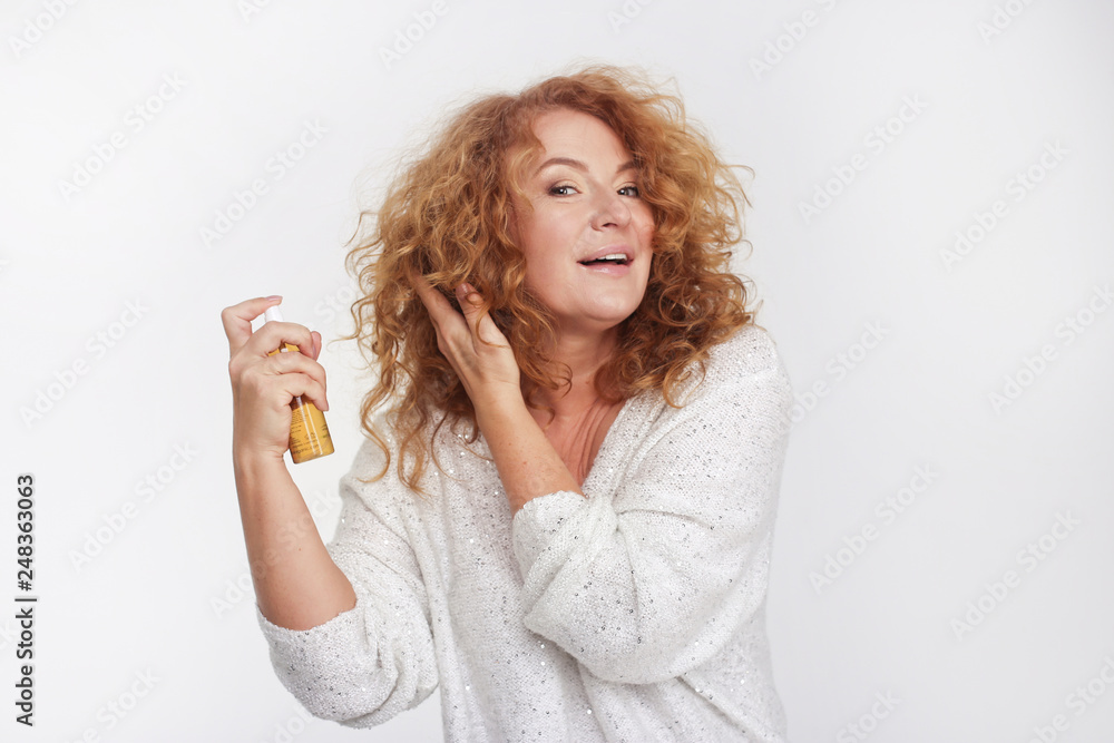 Anti-ageing Concept: Woman In Her Forties caring for curly hair, applying spray on curly red hair Anti-ageing Concept: Woman In Her Forties caring for curly hair, applying spray on curly red hair